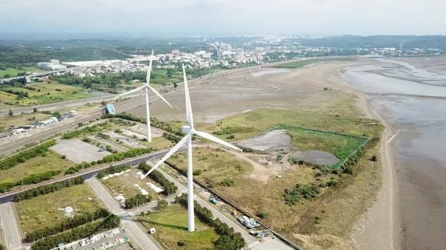 Aerial shot orbiting around two white windmills generating clean energy near Hsinchu City, Taiwan.