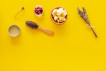 Natural oil for hair. Jojoba, argan, coconut oil near bunch of lavender and hairbrush on yellow background top view copy space