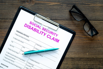 Social security. Disability claim form near glasses on dark wooden background top view