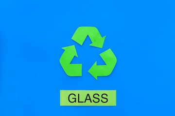 Types of matherial for reycle and reuse. Printed word glass near eco symbol recycle arrows on blue background top view copy space