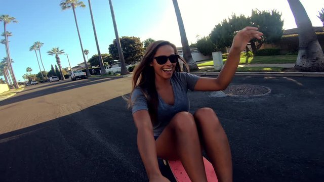 POV happy girl skateboarding down street at sunset holding selfie camera