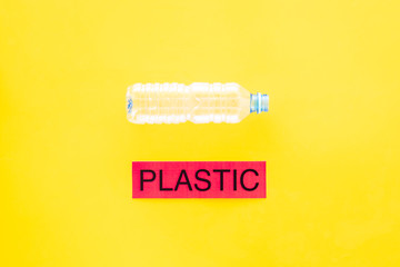 Waste suitable for recycle. Plastic bottle near word plastic on yellow background top view copy space