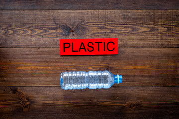 Waste suitable for recycle. Plastic bottle near word plastic on dark wooden background top view copy space
