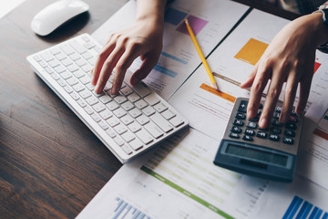 An auditor using a calculator for calculating with financial report and  typing on modern computer keyboard at office.Accounting and technology in office.Finance concept.