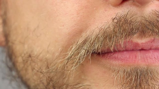 young man touches and twists his mustache and smiles slightly, half front view, macro closeup