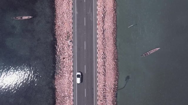 Aerial view of a white car driving on a new road running through shallow sea waters in Jaffna, Sri Lanka