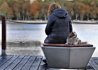 Lonely girl with a dog sitting on the shore of a pond.
