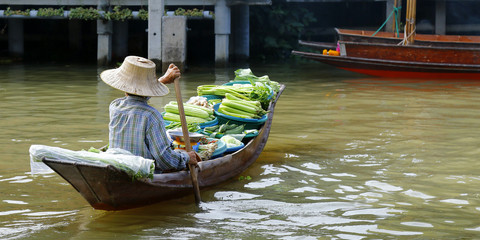 Naklejka premium Woman trading fruit and food in boats at Damnoen Saduak floating market ,Thailand