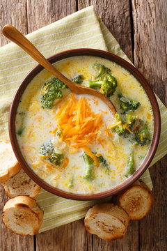 Delicious cheesy broccoli soup with vegetables in a bowl with toast close-up. Vertical top view