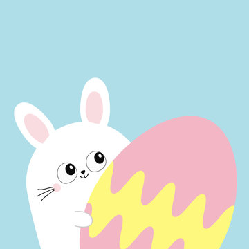 White bunny rabbit holding big painted egg. Happy Easter. Funny head face, eyes, ears. Cute kawaii cartoon character. Baby greeting card. Blue background. Flat design.