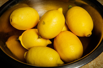 many juicy lemons lie in metal bowl