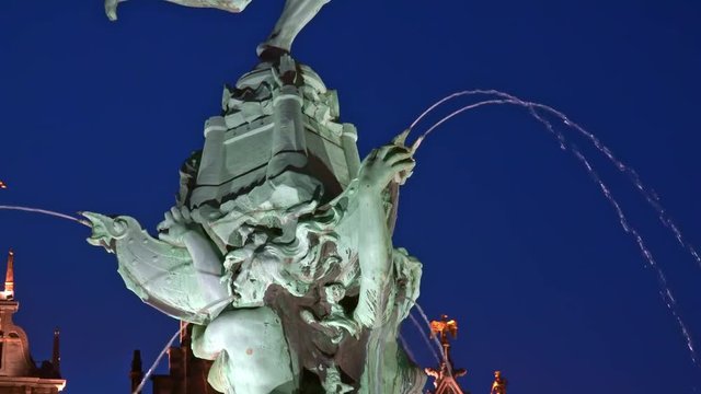Brabo Fountain depicting legendary Flemish hero standing on castle supported by mermaids spouting water illuminated by light at evening. Great Market Square, Antwerp, Belgium. Camera zooms out.