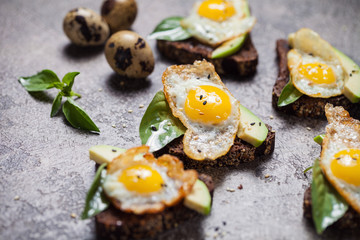 toast brown bread with quail egg and avocado, basil on table