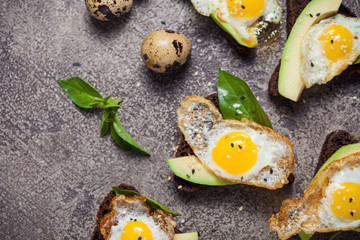toast brown bread with quail egg and avocado, basil on table