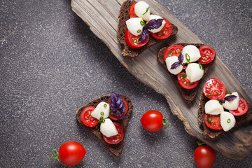 Obraz na płótnie Canvas Bruschetta with mozzarella and tomato with basil on black bread