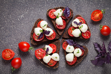 Bruschetta with mozzarella and tomato with basil on black bread