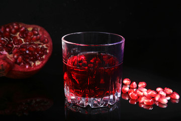 Glass with pomegranate juice Pomegranate seeds and Beautiful ripe pomegranate on black mirror background with place for copy space.