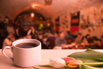 Tea cup with tulips on the wooden table opposite blurred background. Collage. Selective focus. Toned