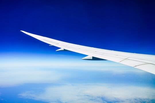 white wing of the aircraft view from airplane window seat flying in the blue sky with white clouds background over the ocean, copy space, travel concept