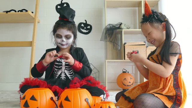 Two asian girl dressed as witch and ghost sitting and eating chocolate together in a room decorated for Halloween
