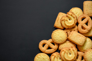 pile of Danish butter cookies in different shape on black board background, copy space