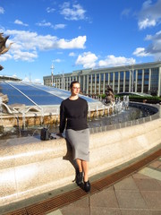 Girl sitting on the fountains in the center of Minsk against the blue sky.
