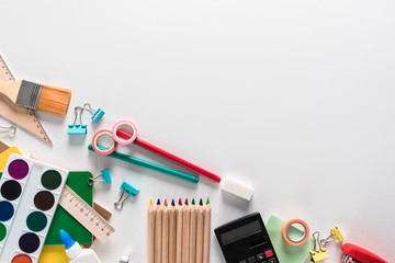 Top view over a school supplies as calculator, rulers, tapes, paper clips, notebooks and other stuff placed at one corner of a white background. Back to school concept. Office supplies flat lay