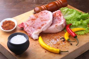 Raw chop on a rustic cutting board with salt, pepper and grinder for spices . for copy space. Top View.
