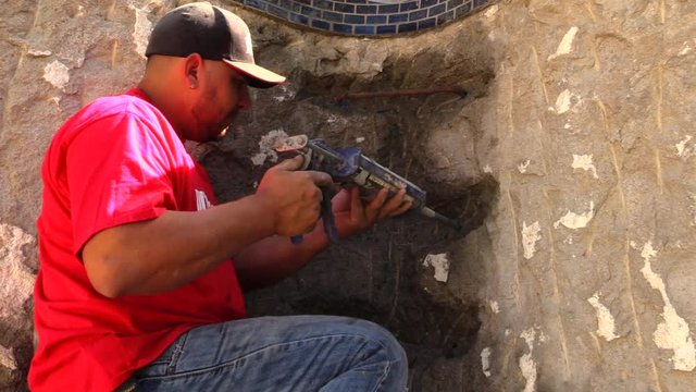 Construction worker injecting glue epoxy into the hole where the rebar will be inserted.