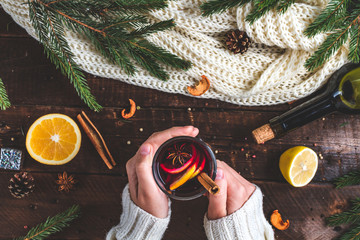 A young woman in a warm, knitted, white pullover is holding a Christmas, hot mulled wine in a glass with spices and citrus fruits. A cozy, winter evening. Winter drinks. Flat lay, top view