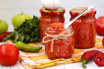 Homemade adjika with tomatoes in an open jar on a white background