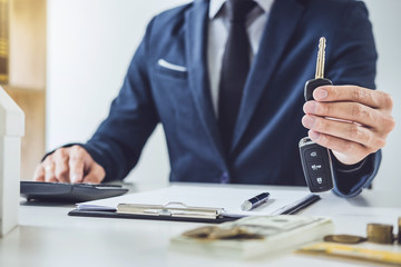 Salesman holding a key and calculating a price of selling new car and home loan, transportation and...