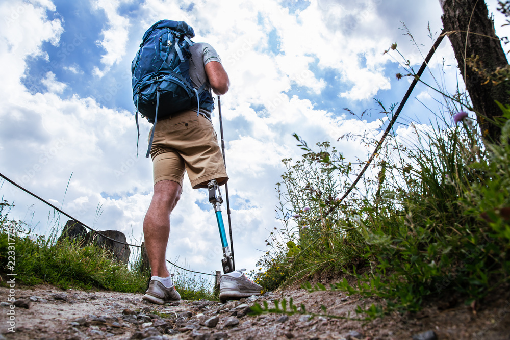 Wall mural Rear view of a young sporty man with prosthesis standing on the path