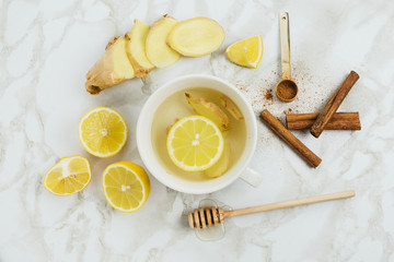Flatlay of healthy drink with lemon, fresh ginger root, cinnamon sticks and agave syrup on marble background, natural cold or sore throat