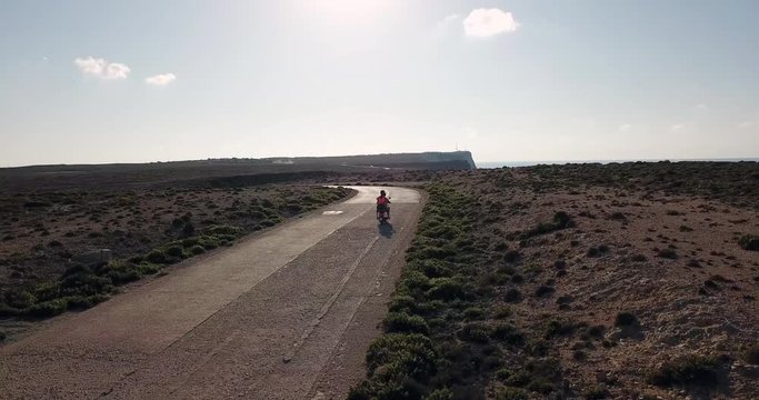 Man and woman riding motorcycle on the street in the island of Lampedusa, Italy during summer holidays with Mediterranean sea in background