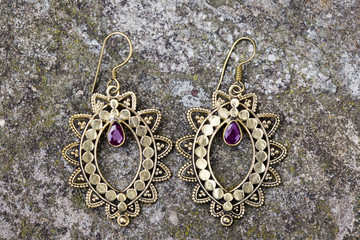 Indian spiritual ornamental style brass earrings on rocky background