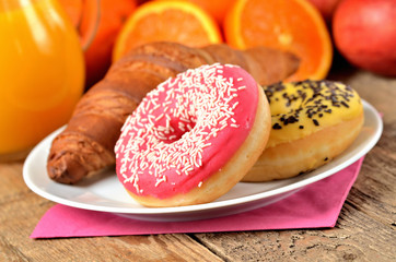 Detail of donuts, orange juice, croissant - sweet breakfast on wooden table