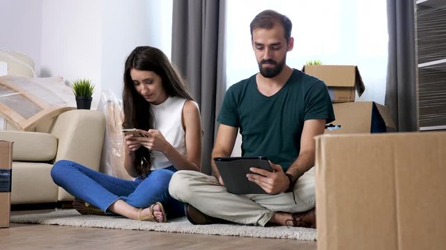 Young couple in their new apartment surrounded by cardboard boxes are shopping online for furniture