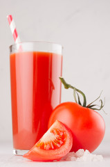 Healthy beverage - fresh vegetable tomato juice, straw, salt and red tomatoes on soft white wood background, macro, vertical.
