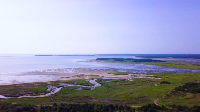 Sunken Meadows on Cape Cod, MA. The marsh and channels of water connect to the bay. The tide is low and much of the beach is freshly exposed. The camera pans to the right as it descends.