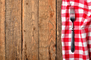 Fork on red checkered tablecloth right frame on vintage wooden table background - view from above