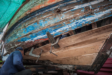 Mechanic maintenance old wood boat on beach with hand, fishery traditional Thailand bay