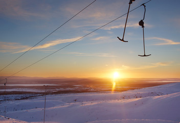 Two hooks are hanging on a lift cable in a ski resort in winter with a beautiful sunset sky