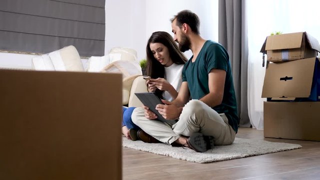 Revealing shot young beautiful inlove couple just moved in new house. They are sitting on the floor shopping online for furniture
