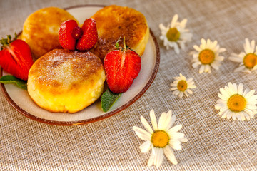 A large plate with curd cheese for breakfast, Cottage cheese pancakes, curd fritters with fresh berries strawberries with daisy flowers