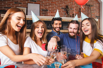 Group of multicultural friends in a party hats cheering with champagne