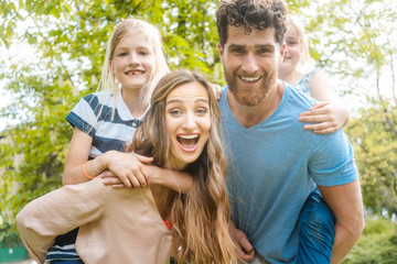 Fototapeta premium Family of four having fun, daddy and mommy are carrying the kids piggyback
