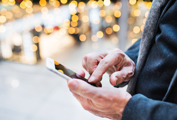 Senior man with smartphone in shopping centre at Christmas time.