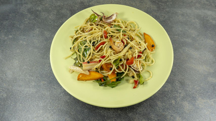 Spaghetti seafood in a green plate on a black stone floor table, front view with copy space for your text.