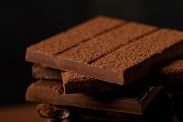 close-up view of delicious assorted chocolate bars with cocoa powder on black